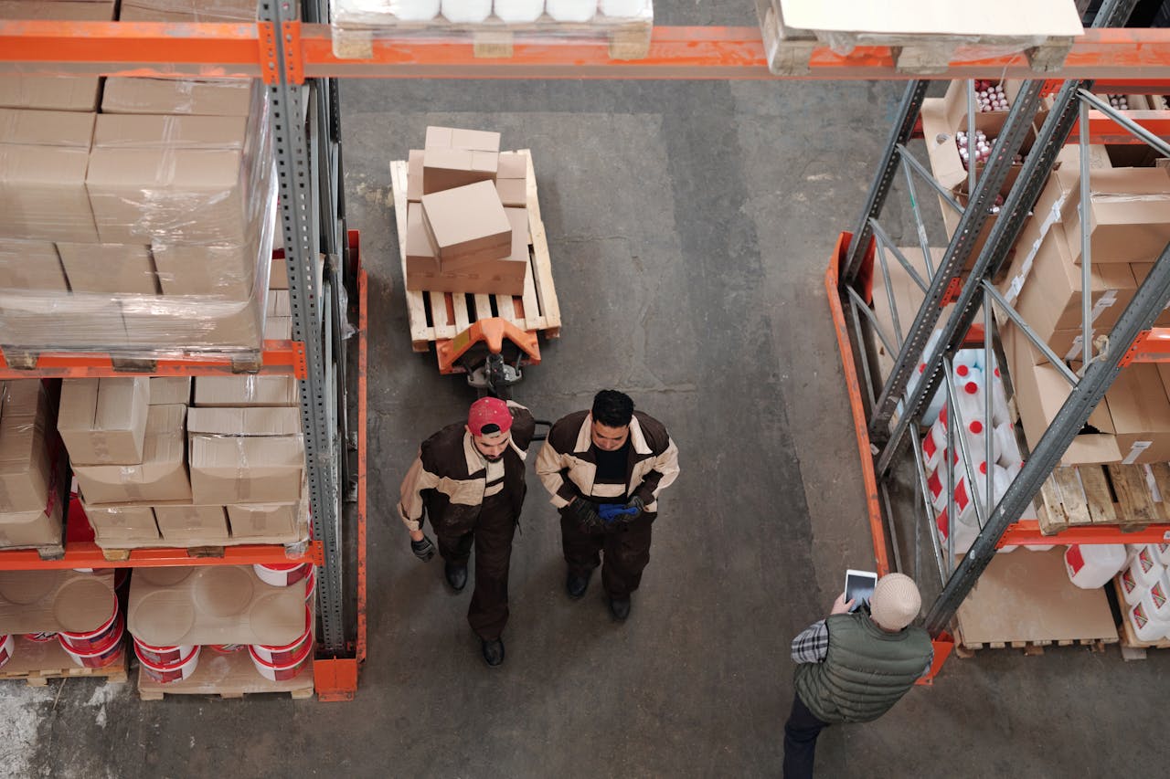Two logistics professionals walking through a spacious warehouse filled with shelves and inventory.